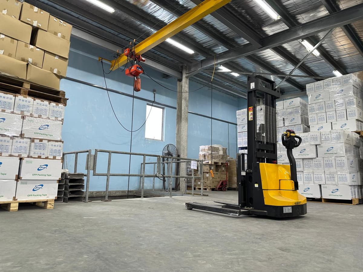 Megapac warehouse — electric pallet stacker and overhead jib crane beside cartons of OPP tape